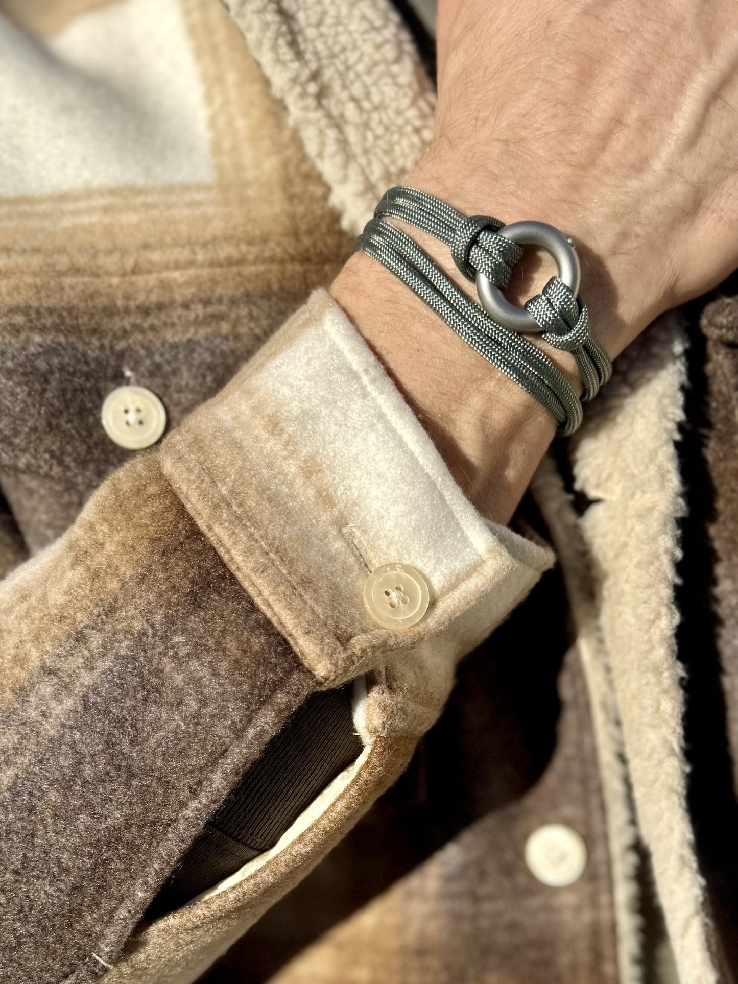Close-up of a brown coat with a button and a wrist wearing a green urn ashes bracelet.